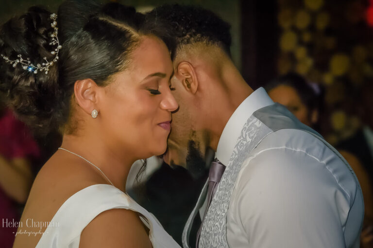 A bride and groom share a tender moment, their foreheads touching affectionately, as they smile gently at each other during their wedding reception.