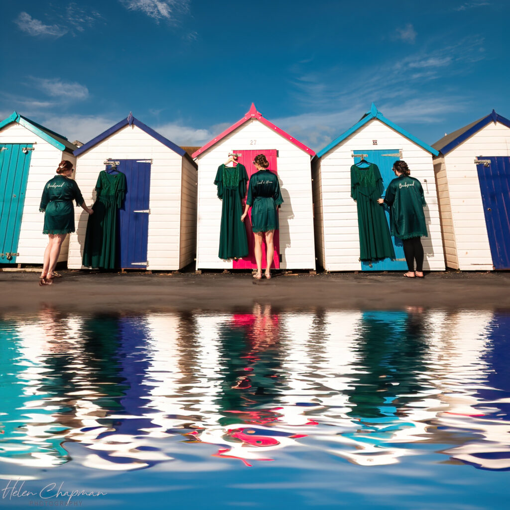 Colorful beach huts reflected in water, people in robes standing.