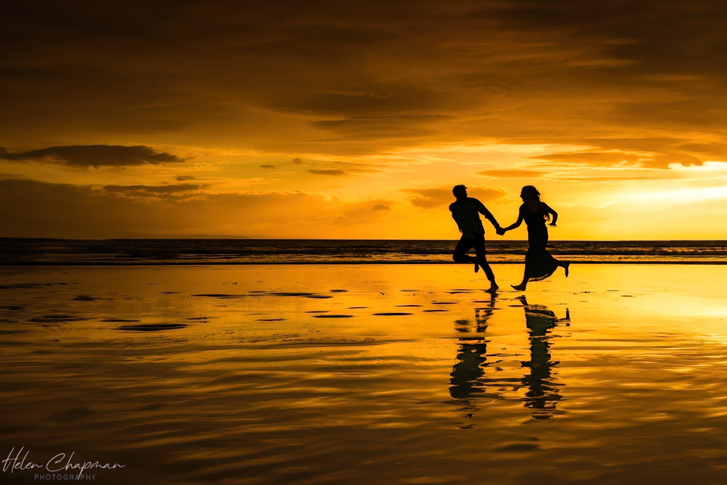 Couple running on beach at sunset with reflections.