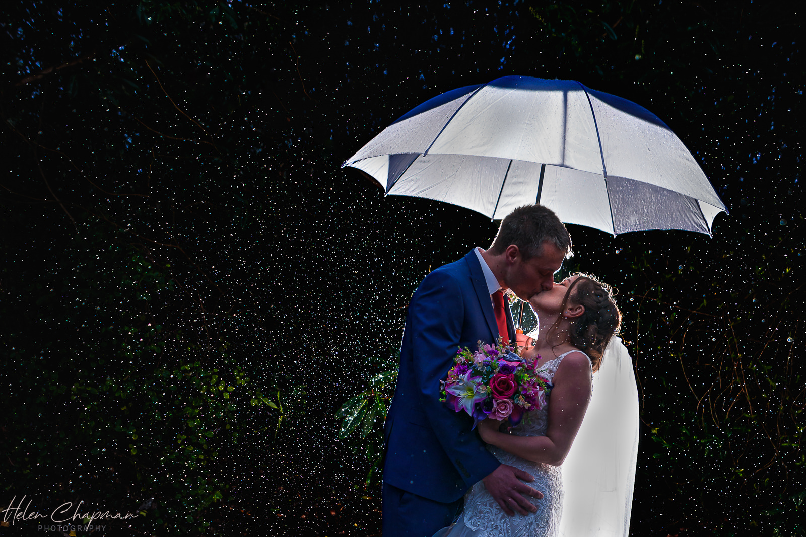 Couple kissing under umbrella at night rain.
